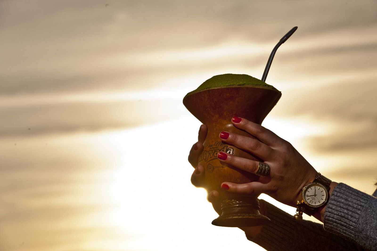 Mão erguendo a cuia de erva-mate contra o sol